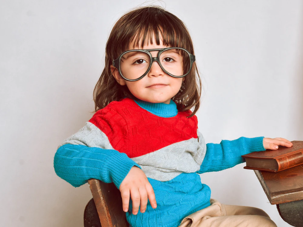 Niña con gafas de montura roja sentada en una silla de madera